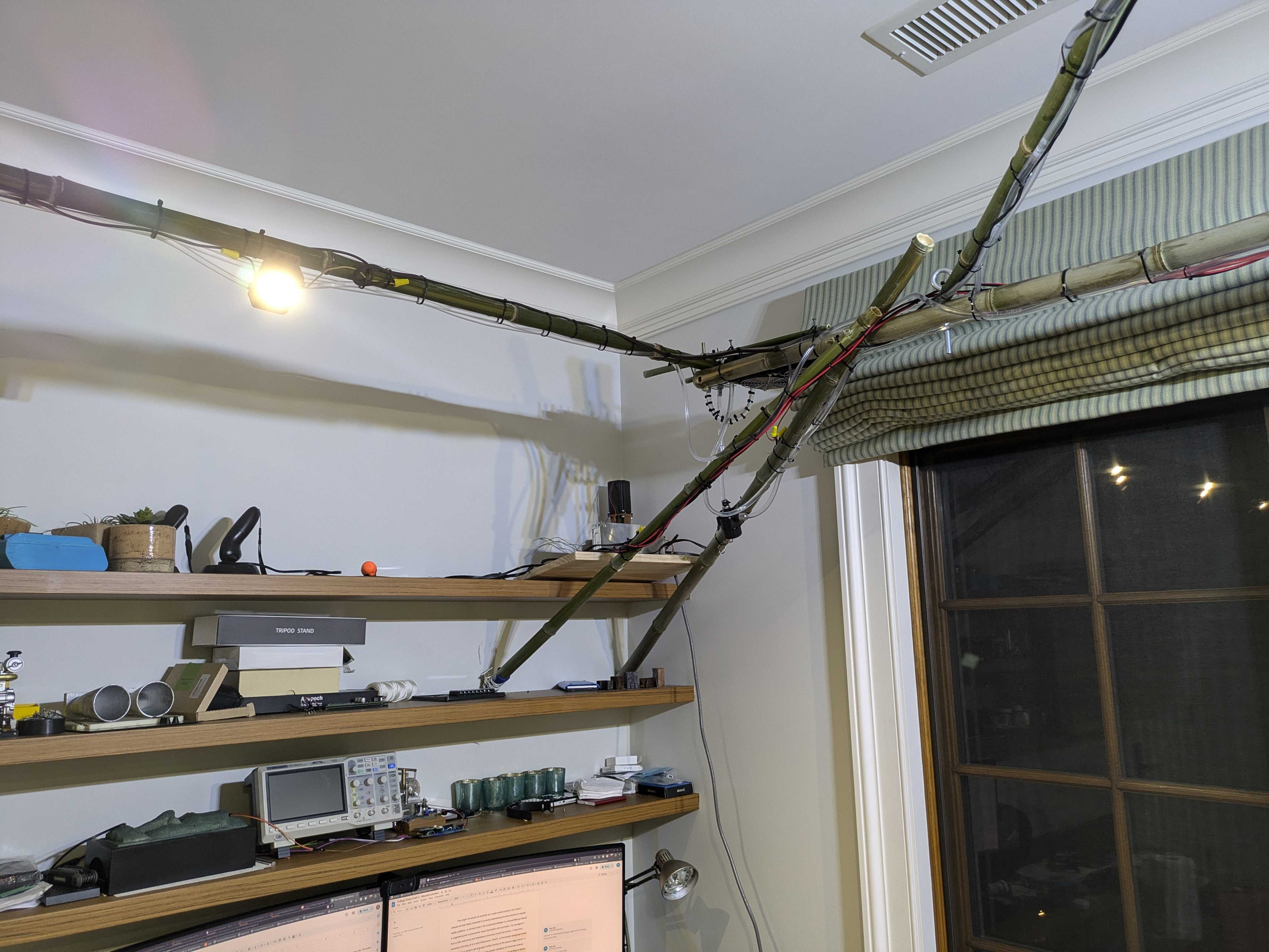 far-away view of a bamboo scaffold upon which several lines of PVC and low-gauge wire run across