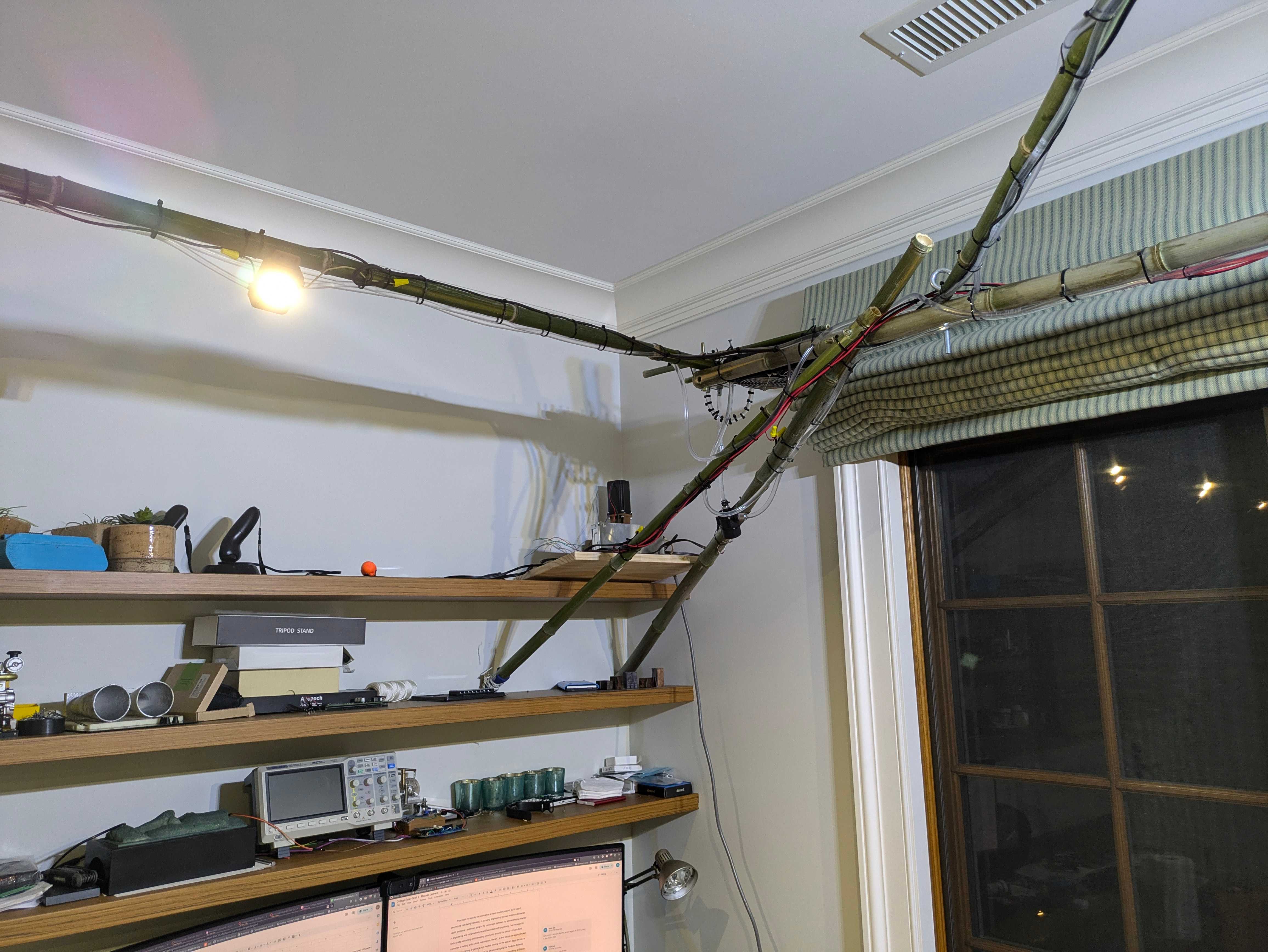 far-away view of a bamboo scaffold upon which several lines of PVC and low-gauge wire run across