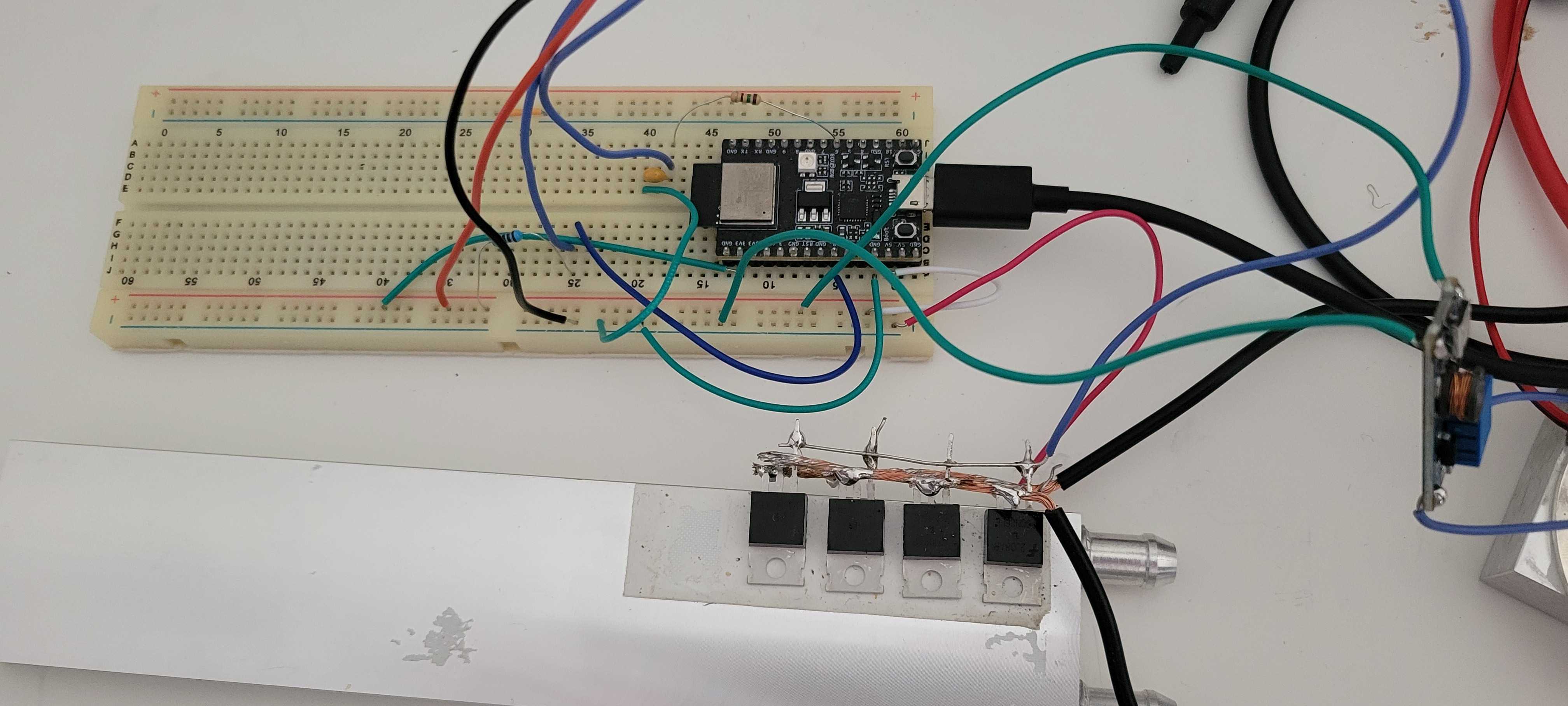 a breadboard with an esp32-c3 devboard and some resistors and capacitors wired into it. in the lower half of the image, there's an aluminum watercooling block with some mosfets mounted to it